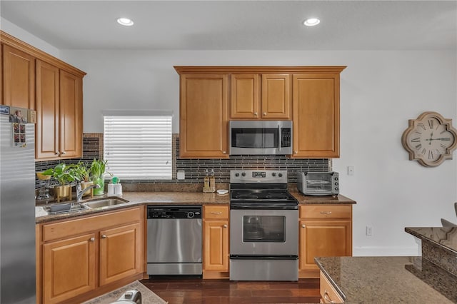kitchen featuring dark stone counters, dark wood-style flooring, a sink, stainless steel appliances, and decorative backsplash