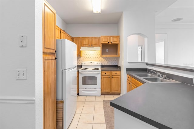 kitchen featuring light tile patterned floors, white appliances, under cabinet range hood, a sink, and dark countertops