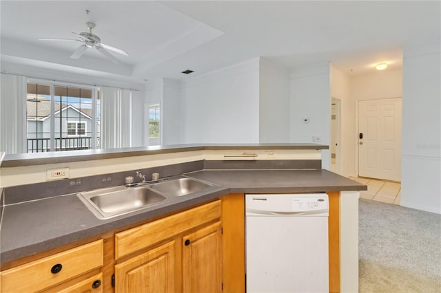 kitchen with a tray ceiling, a ceiling fan, dishwasher, a sink, and dark countertops