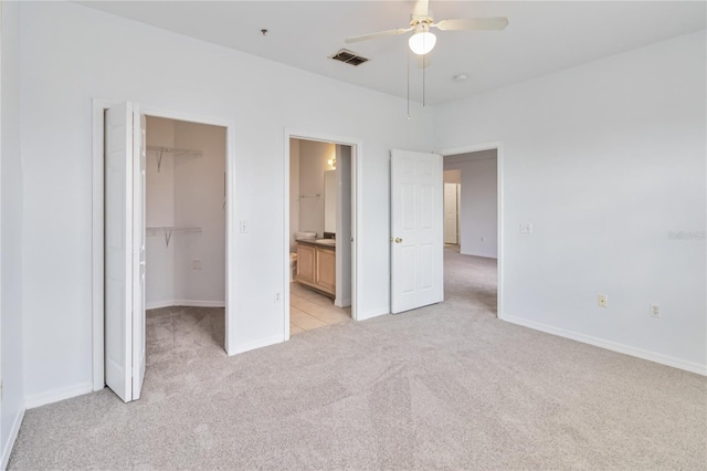 unfurnished bedroom featuring a closet, baseboards, light carpet, a walk in closet, and visible vents