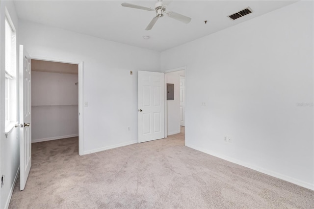 unfurnished bedroom with visible vents, baseboards, electric panel, a walk in closet, and light carpet