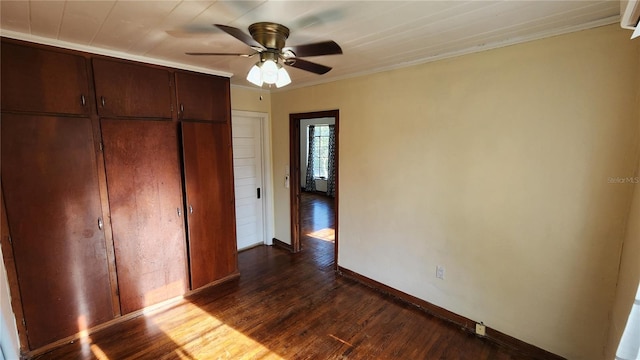 unfurnished bedroom with a closet, dark wood-style flooring, baseboards, and ornamental molding