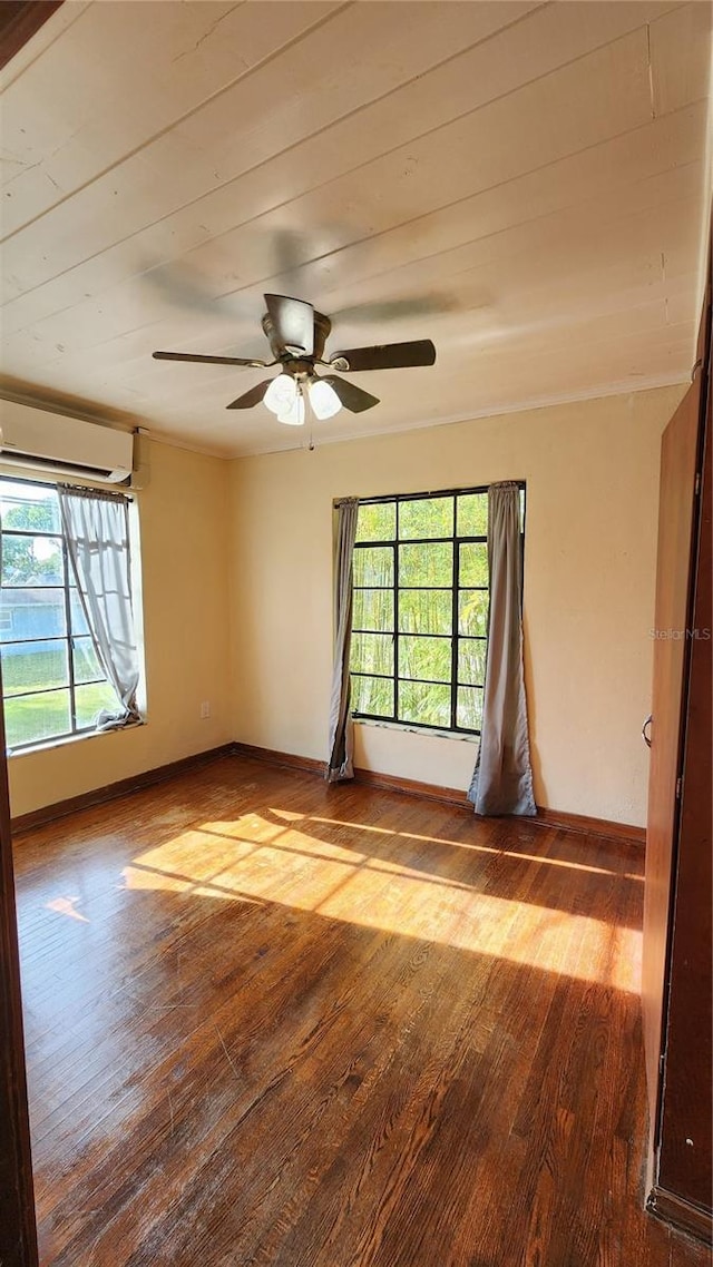 unfurnished room featuring a wall unit AC, wood finished floors, ceiling fan, and baseboards