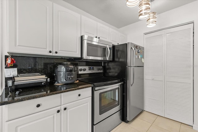 kitchen with dark stone countertops, backsplash, light tile patterned flooring, white cabinets, and stainless steel appliances