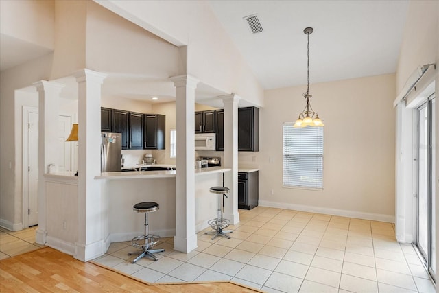 6959 Brescia Way, Orlando, FL 32819 - kitchen with light countertops, freestanding refrigerator, white microwave, and decorative columns