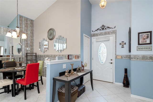 tiled foyer entrance featuring high vaulted ceiling, an inviting chandelier, and wainscoting