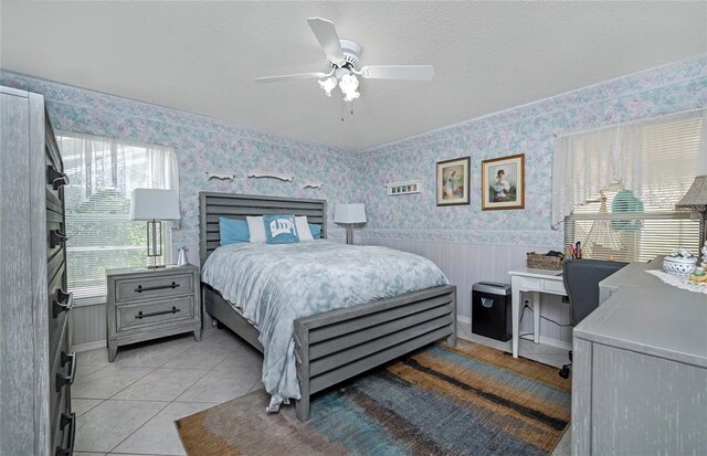 bedroom with ceiling fan, a wainscoted wall, light tile patterned flooring, wallpapered walls, and baseboards