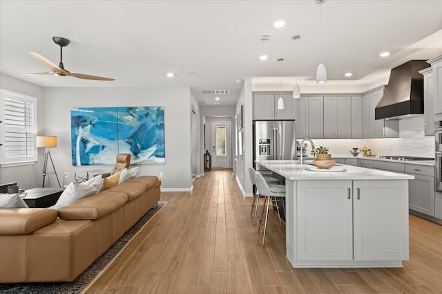 kitchen with a breakfast bar area, gray cabinetry, visible vents, open floor plan, and wall chimney exhaust hood