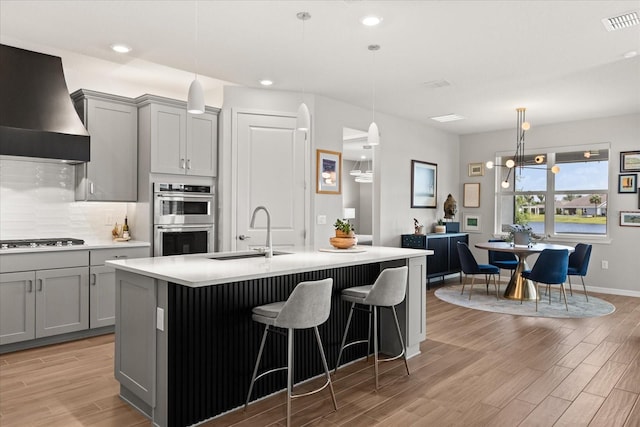 kitchen featuring gray cabinetry, stainless steel double oven, custom range hood, and a sink