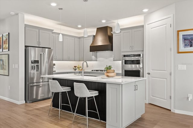 kitchen with baseboards, light wood finished floors, a sink, custom range hood, and appliances with stainless steel finishes
