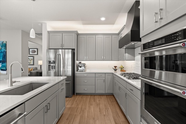 kitchen featuring stainless steel appliances, wall chimney exhaust hood, gray cabinetry, and a sink