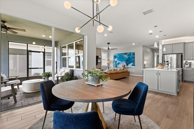 dining space with light wood-style flooring, visible vents, and ceiling fan with notable chandelier