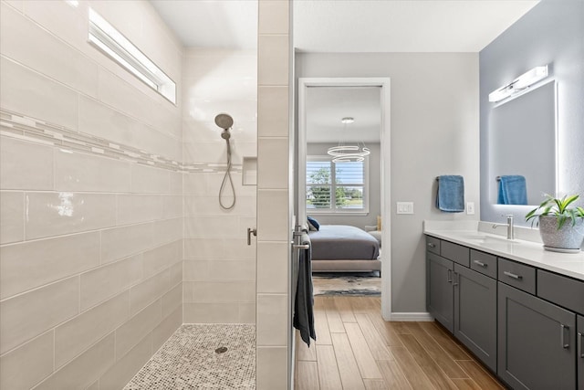 ensuite bathroom with wood finished floors, tiled shower, baseboards, ensuite bath, and vanity