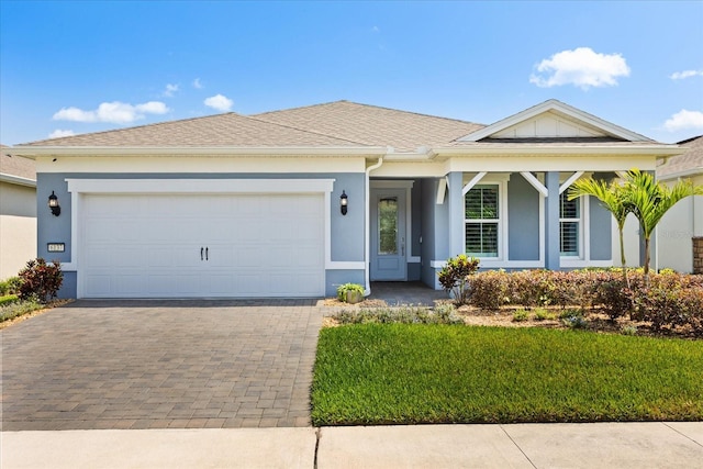 single story home featuring an attached garage, stucco siding, decorative driveway, and a front yard