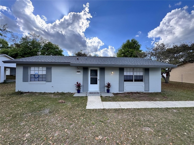 ranch-style home with concrete block siding, a shingled roof, and a front yard