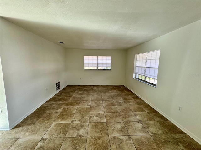 spare room with stone finish flooring, baseboards, a textured ceiling, and visible vents
