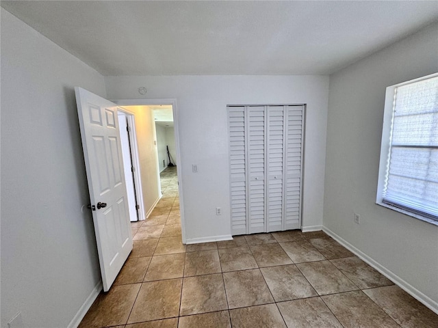 unfurnished bedroom featuring baseboards, tile patterned flooring, and a closet