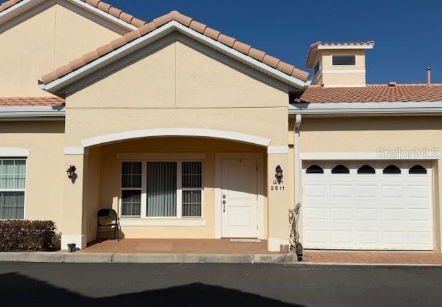 mediterranean / spanish house with a garage, stucco siding, and a tiled roof