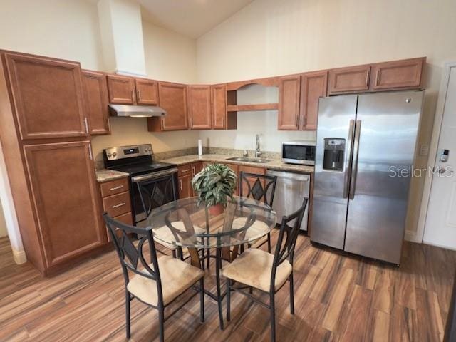 kitchen featuring a towering ceiling, a sink, under cabinet range hood, stainless steel appliances, and dark wood-type flooring