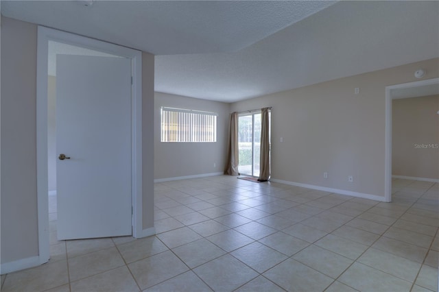 spare room with light tile patterned floors, baseboards, and a textured ceiling
