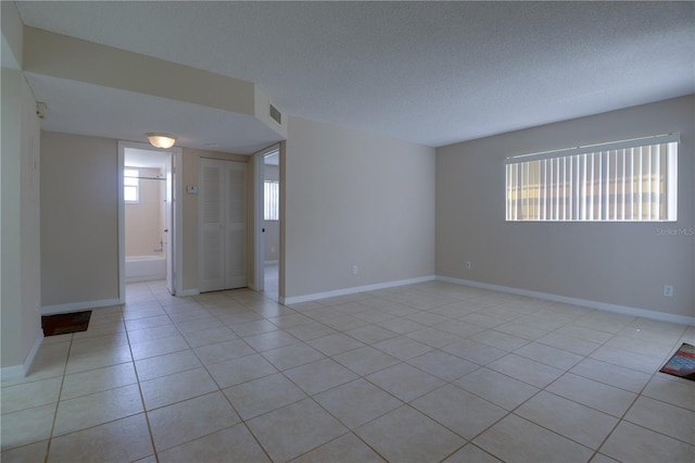 spare room with visible vents, a textured ceiling, baseboards, and light tile patterned flooring
