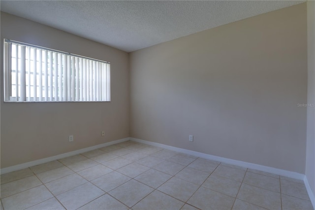 spare room featuring light tile patterned floors, baseboards, and a textured ceiling