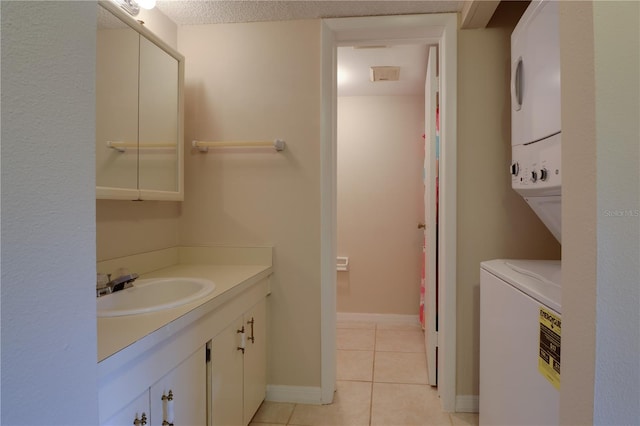 bathroom with tile patterned flooring, vanity, stacked washer / dryer, and baseboards
