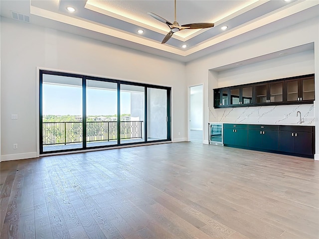 1080 E Jack Nicklaus Ct, Kissimmee, FL 34747 - unfurnished living room featuring wine cooler, baseboards, a ceiling fan, a tray ceiling, and light wood-style flooring