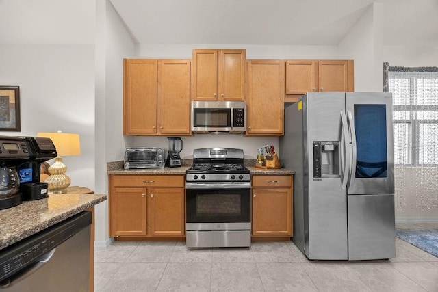 kitchen with light stone countertops, appliances with stainless steel finishes, light tile patterned flooring, baseboards, and a toaster