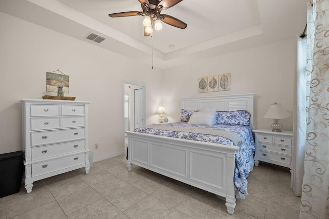 bedroom with light tile patterned floors, visible vents, a tray ceiling, and a ceiling fan
