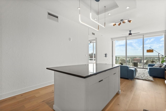 kitchen with open floor plan, light wood-style flooring, dark countertops, white cabinetry, and a center island