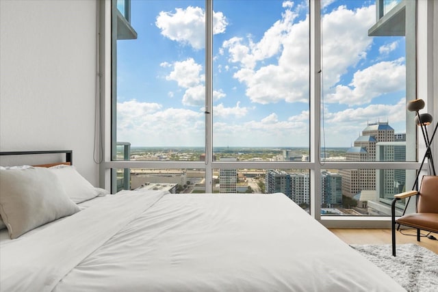 bedroom featuring multiple windows, a city view, wood finished floors, and a wall of windows