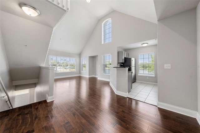 unfurnished living room featuring high vaulted ceiling, baseboards, and wood finished floors