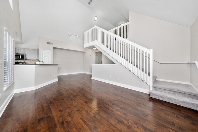 unfurnished living room with high vaulted ceiling, dark wood finished floors, visible vents, and stairs