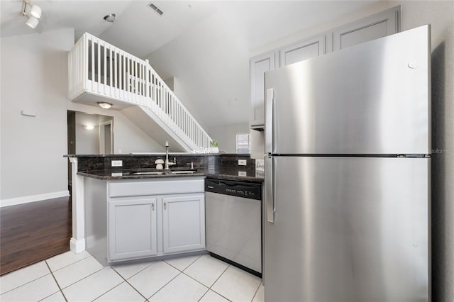 kitchen featuring dark stone countertops, a peninsula, light tile patterned floors, stainless steel appliances, and a sink