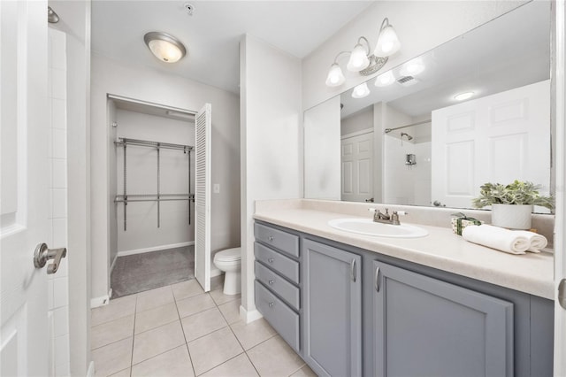 full bathroom featuring tiled shower, vanity, tile patterned flooring, toilet, and a walk in closet