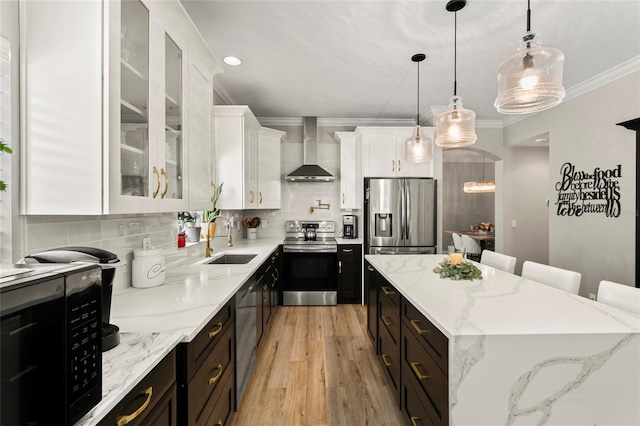 kitchen featuring stainless steel appliances, a sink, a kitchen island, wall chimney exhaust hood, and white cabinetry