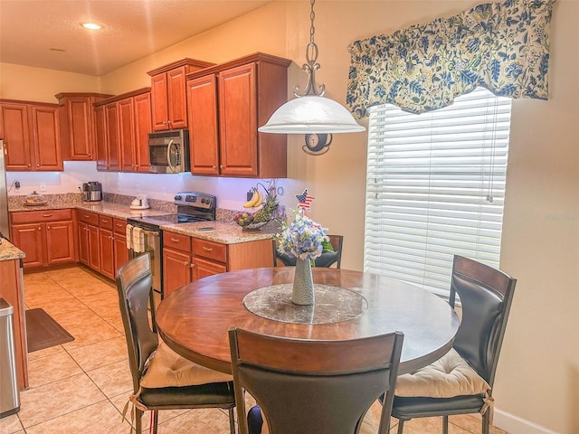 987 Alston Bay Blvd, Apopka, FL 32703 - kitchen featuring light stone counters, brown cabinetry, decorative light fixtures, appliances with stainless steel finishes, and light tile patterned flooring