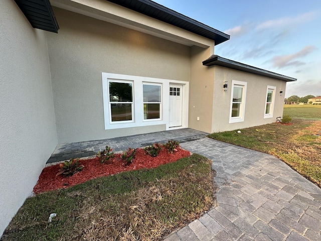 doorway to property with a lawn and stucco siding