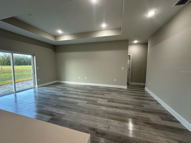 spare room featuring dark wood-style flooring, a tray ceiling, baseboards, and visible vents