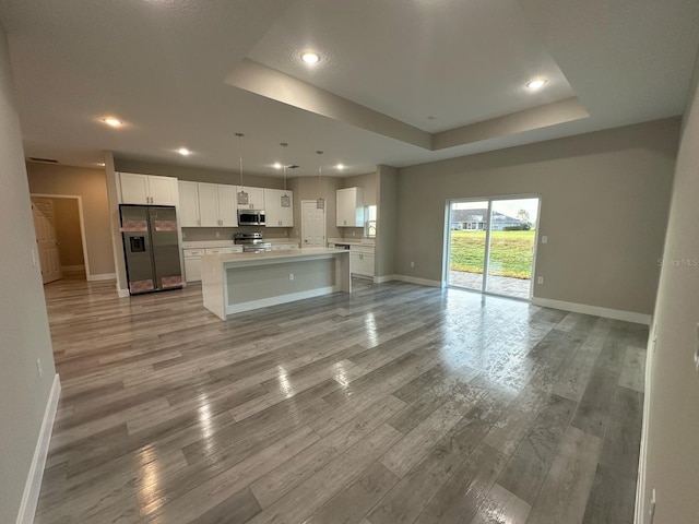 kitchen with light wood-style flooring, white cabinets, stainless steel appliances, a raised ceiling, and open floor plan