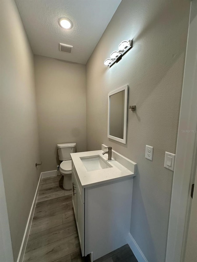 bathroom featuring a textured ceiling, vanity, toilet, wood finished floors, and baseboards