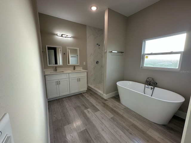 bathroom with a soaking tub, wood finished floors, a sink, a marble finish shower, and double vanity