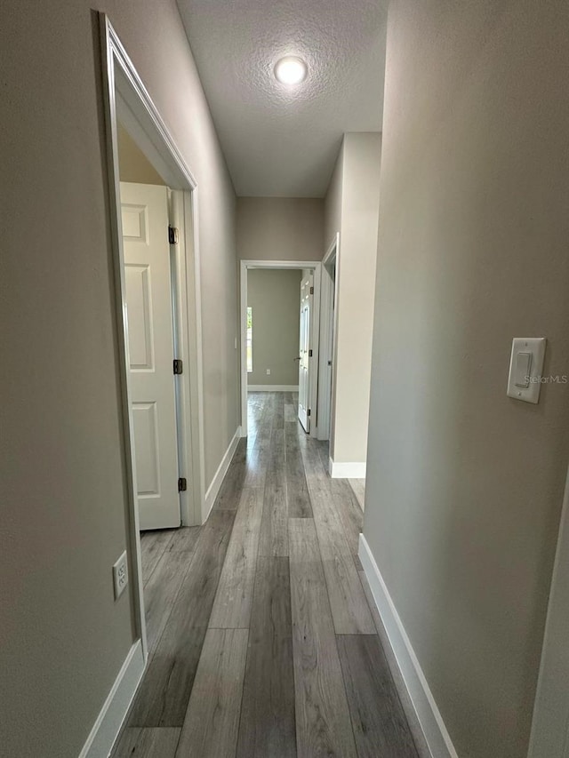hallway featuring a textured ceiling, baseboards, and wood finished floors