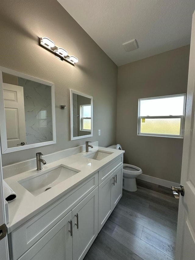bathroom with toilet, wood finished floors, double vanity, and a sink