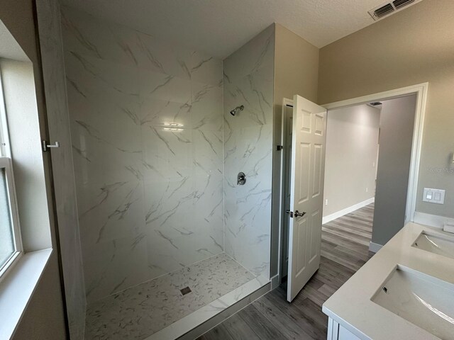 bathroom featuring double vanity, a marble finish shower, visible vents, a sink, and wood finished floors