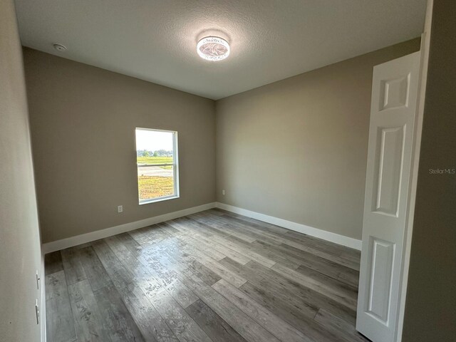 unfurnished room featuring baseboards, wood finished floors, and a textured ceiling