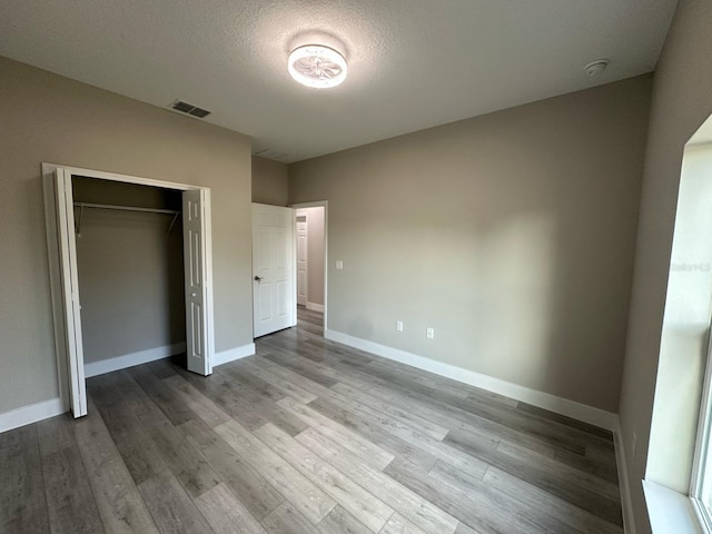 unfurnished bedroom with visible vents, baseboards, a closet, a textured ceiling, and wood finished floors