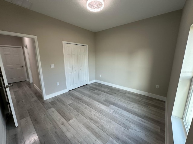 unfurnished bedroom featuring wood finished floors, baseboards, and a closet