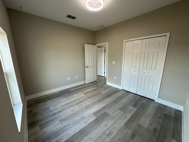 unfurnished bedroom featuring a closet, visible vents, baseboards, and wood finished floors